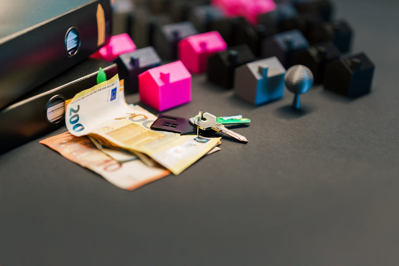 Miniature houses, euro bills, and a house key symbolize real estate investment and property transactions.