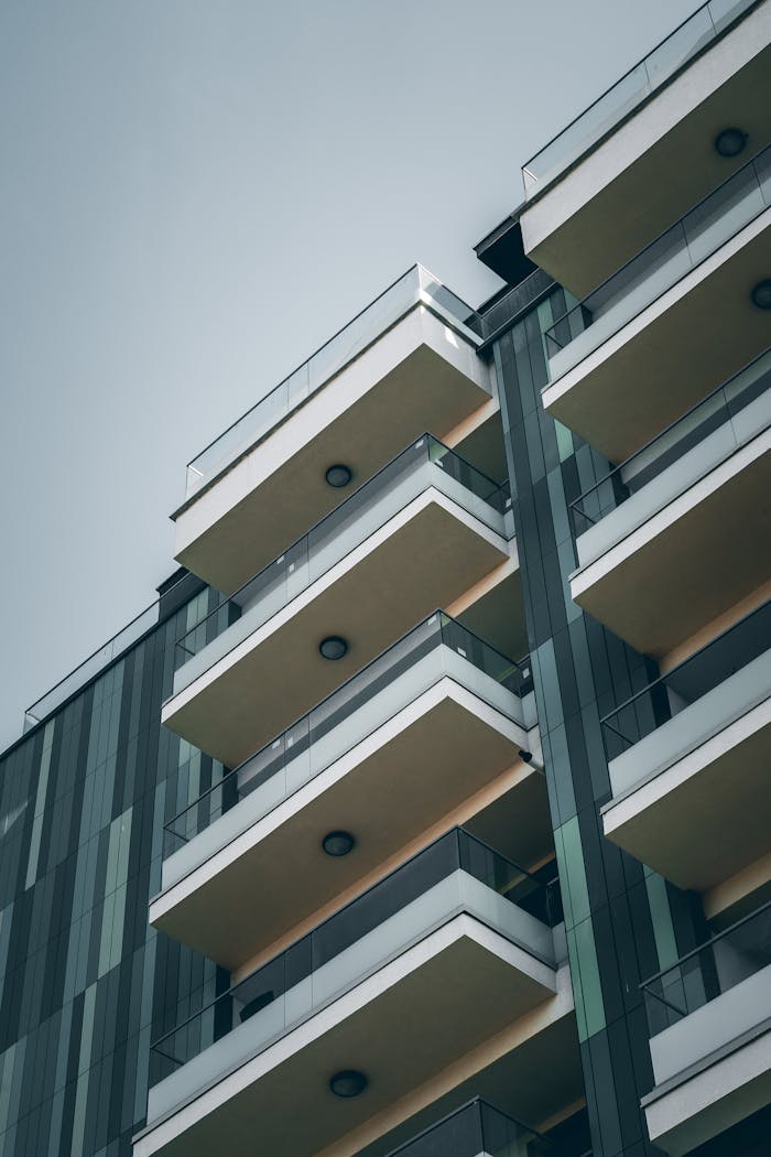 From below facade of contemporary building with geometric pattern and glass balconies against cloudless blue sky